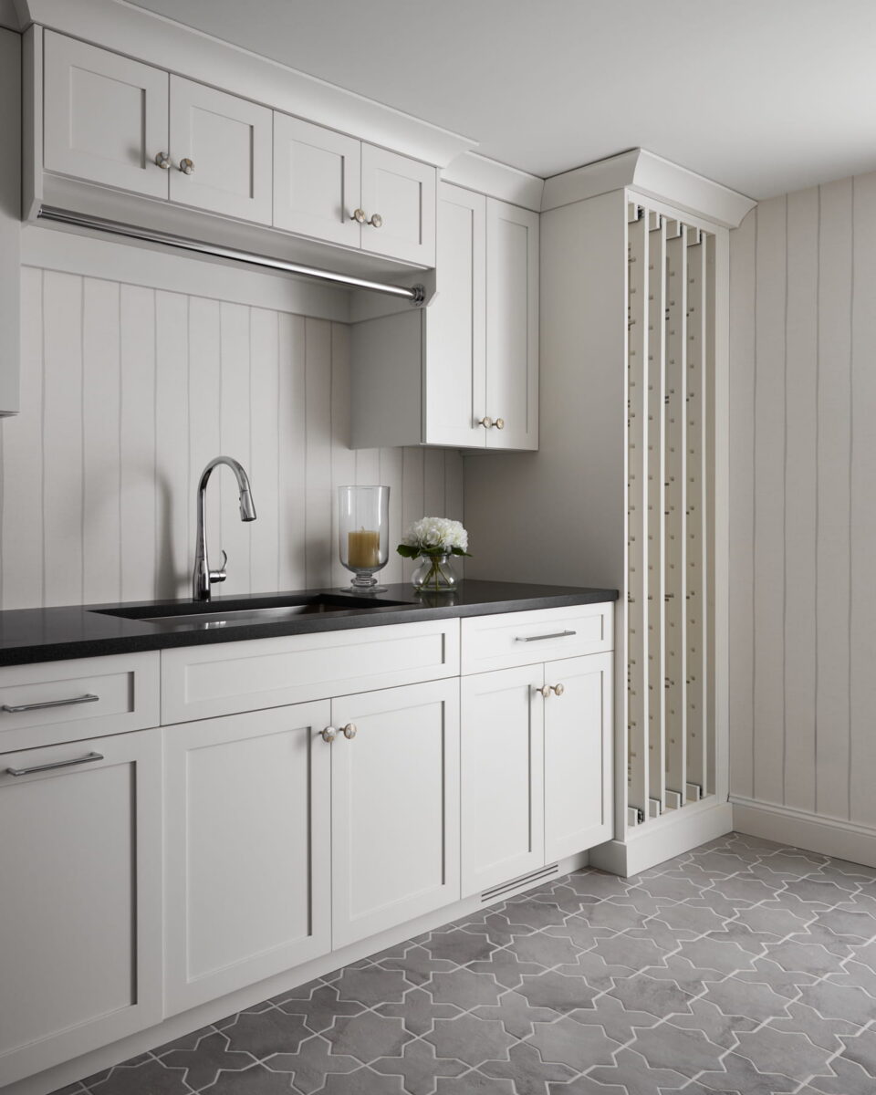 Modern kitchen with white cabinets, black countertop, stainless steel faucet, and decorative items including a glass with a candle and a small white flower arrangement. The floor has a gray geometric tile pattern.